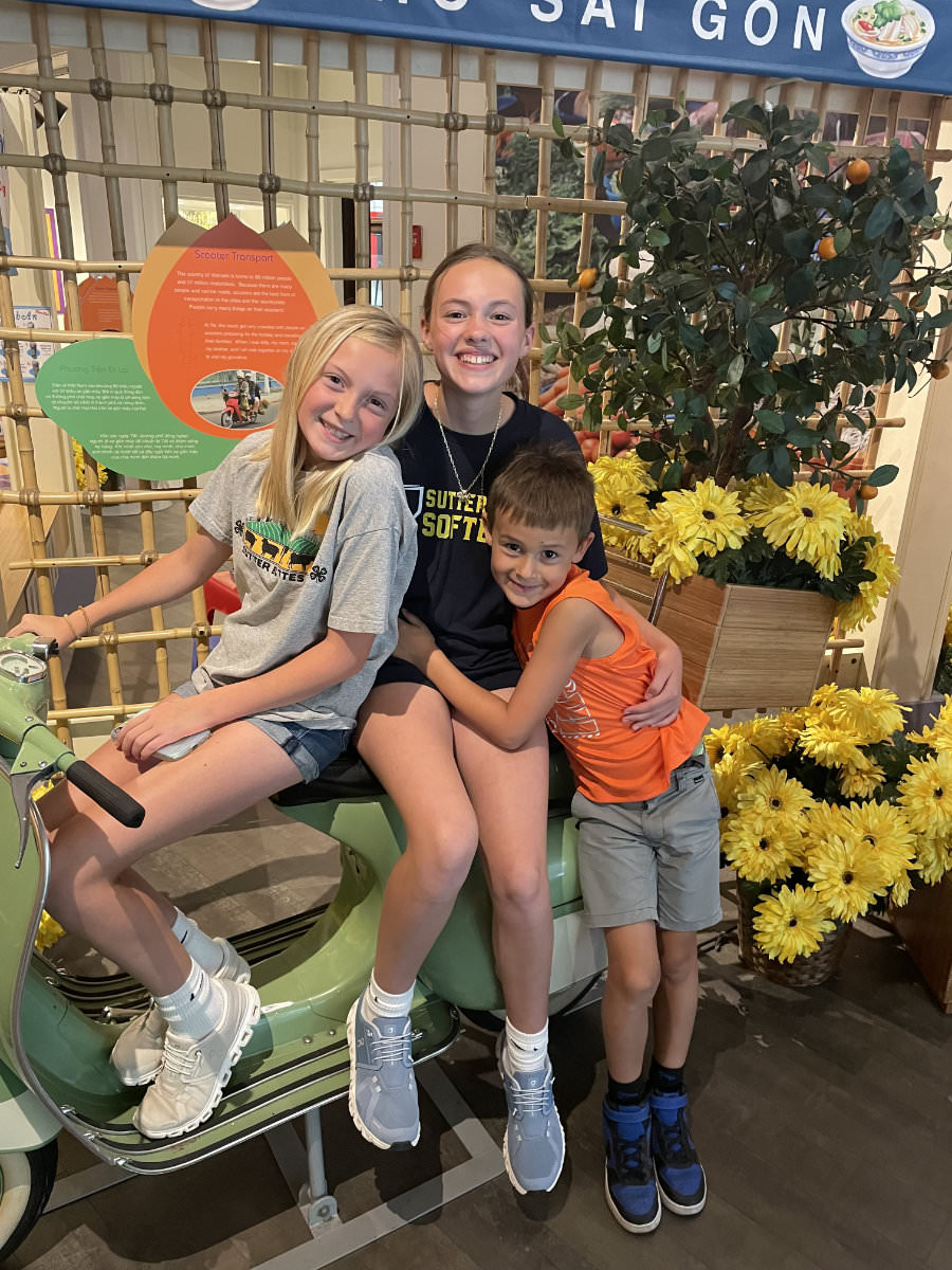 Three children posing on a Vespa in the temporary Voyage to Vietnam exhibit during summer 2025